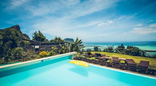 a pool with chairs and the ocean in the background at Hotel Chalets Chamarel in Chamarel