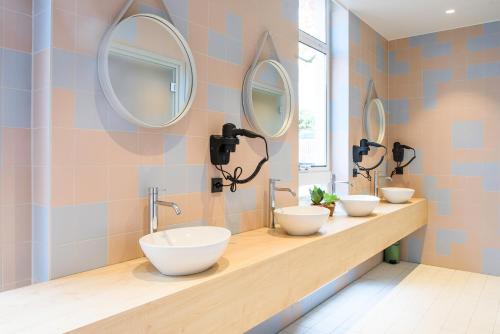 three sinks in a bathroom with three mirrors at The Green Elephant Hostel & Spa in Maastricht