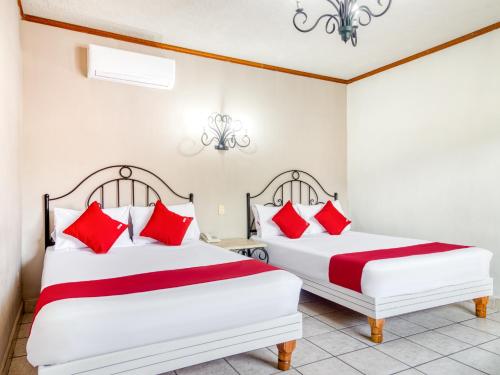 two beds in a room with red pillows at Capital O Hotel La Siesta, Gomez Palacio in Gómez Palacio