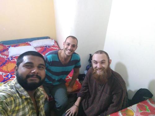 three men sitting on a bed in a room at Atathi Niwas Guest House for Backpackers and Travellers in Siliguri
