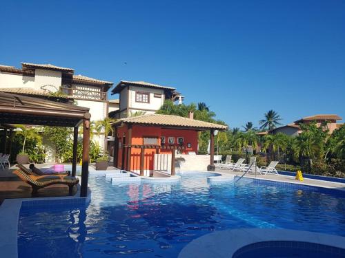 a pool at a resort with chairs and a house at Porto das Baleias Praia do Forte in Praia do Forte
