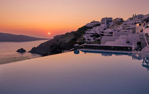boats are docked in the water at sunset at La Perla Villas and Suites - Adults Only in Oia