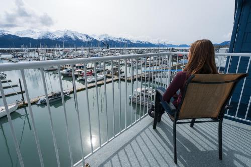 a woman sitting in a chair on a balcony overlooking a marina at Harbor 360 Hotel Seward in Seward