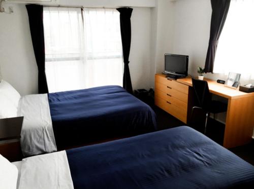 a bedroom with two beds and a desk and a window at HOTEL LiVEMAX BUDGET Fuchu in Fuchu