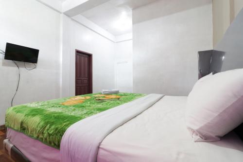 a white bedroom with a bed with a green blanket at Villa Keluarga Bre Batunanggar in Berastagi