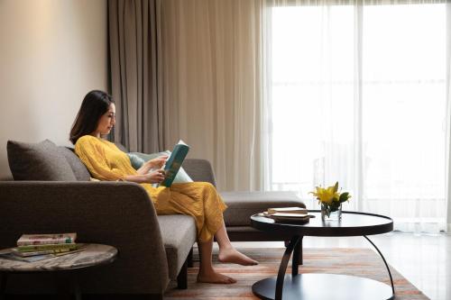 a woman sitting on a couch with a laptop at Oakwood Residence Hanoi in Hanoi