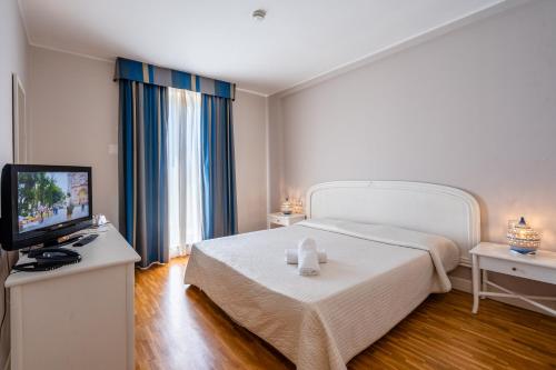 a bedroom with a white bed and a television at Capo Peloro Hotel in Torre Faro