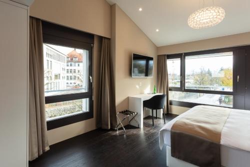 a bedroom with a bed and a desk and windows at Hotel Lo! im Kreuz Jona in Rapperswil-Jona