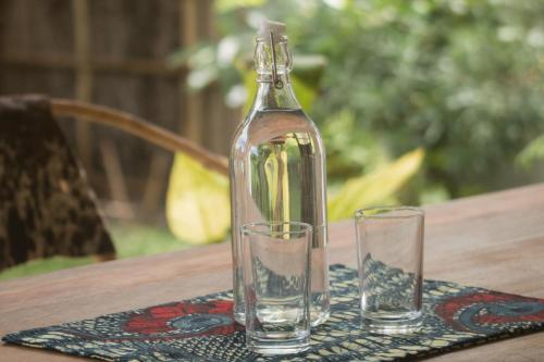 a glass bottle and two glasses on a table at Villa Kiota in Paje