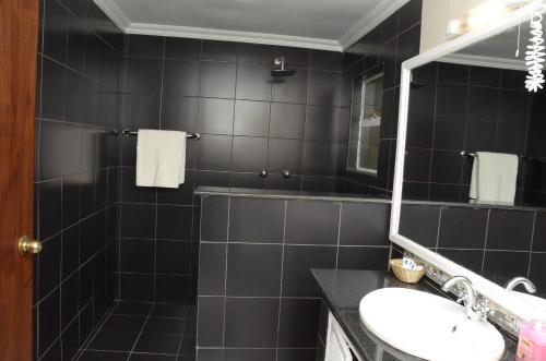 Baño de azulejos negros con lavabo y espejo en The Noble Hotel & Conference Centre en Eldoret