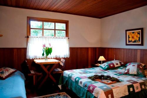 1 dormitorio con cama, mesa y ventana en Pousada Vale das Hortensias, en Visconde De Maua