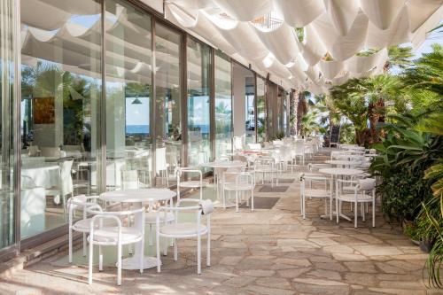 a restaurant with white chairs and tables and windows at Hotel Caravelle Thalasso & Wellness in Diano Marina