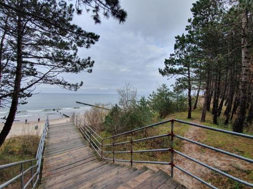 Una pasarela de madera que conduce a una playa con árboles. en DWIE SOSNY - Apartament Morski Kryształ - SAUNA, JACUZZI, SIŁOWNIA, BAWIALNIA - 365PAM, en Ustronie Morskie