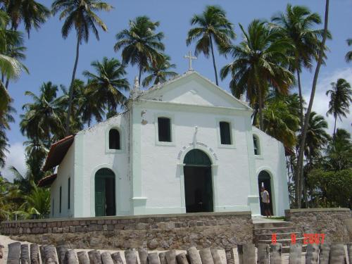 a small white church with palm trees in the background at Privê dos Carneiros in Tamandaré