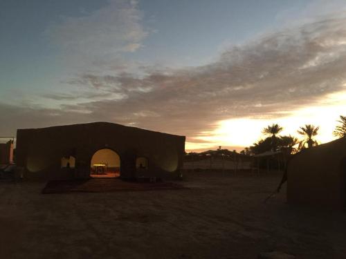 a building in the desert with the sunset in the background at Camp Sahara inspiration in Mhamid