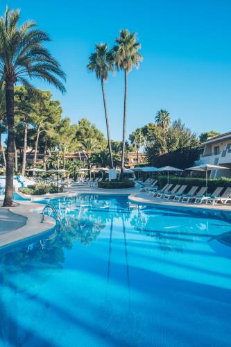 a swimming pool with palm trees and chairs at Iberostar Waves Pinos Park in Font de Sa Cala