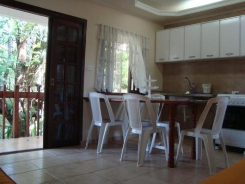 a kitchen with white chairs and a table and a kitchen with a window at Budget Apartamento Na Praia Ubatuba in Ubatuba