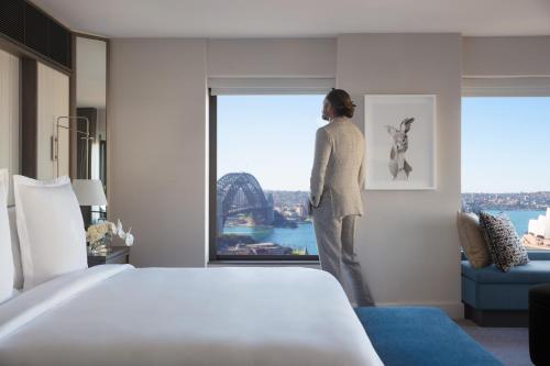 a man standing in front of a window looking at the ocean at Four Seasons Hotel Sydney in Sydney