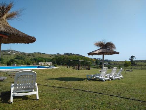 four white chairs and an umbrella next to a pool at Cabañas Calihue in Tandil