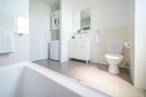 a white bathroom with a toilet and a bath tub at Mantra Wollongong in Wollongong