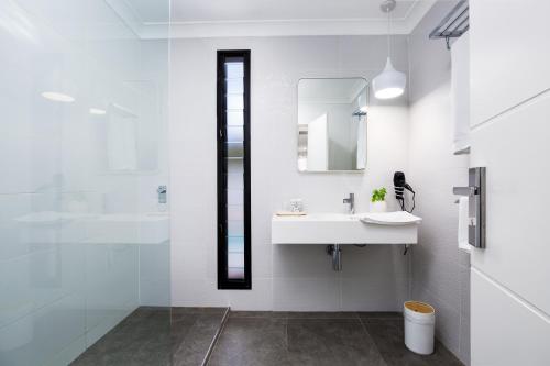 Baño blanco con lavabo y espejo en Lamour Holiday Beach House, en Gold Coast