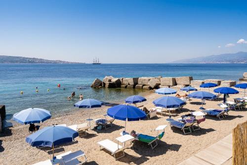 a beach with blue umbrellas and people in the water at Capo Peloro Hotel in Torre Faro
