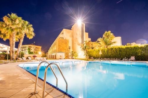 a swimming pool with a building in the background at Capo Peloro Hotel in Torre Faro
