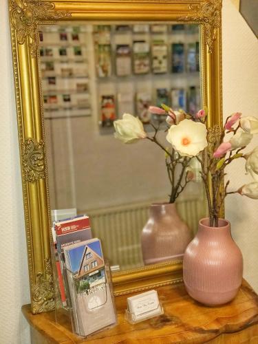 a mirror and a vase with flowers on a table at Pension Trautheim - Am Stadtpark in Bad Harzburg
