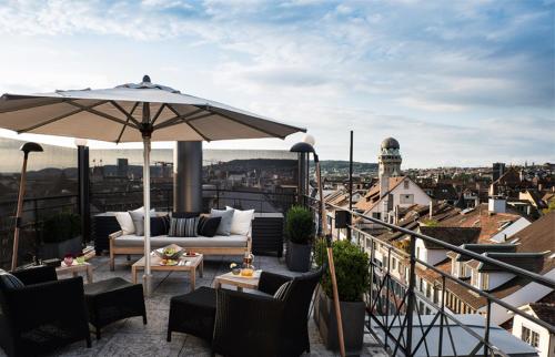 eine Terrasse mit einem Sofa und einem Sonnenschirm auf dem Balkon in der Unterkunft Widder Hotel - Zurichs luxury hideaway in Zürich