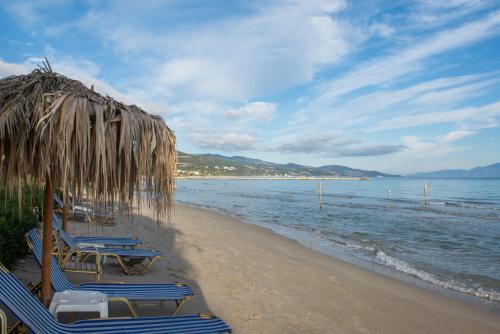 a beach with chairs and a straw umbrella and the ocean at VillaPouliezos Apartments in Alikanas
