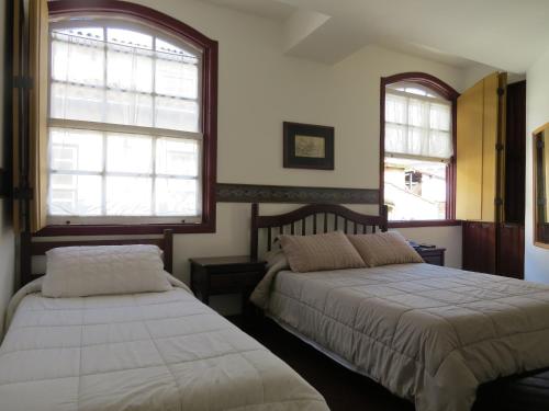 a bedroom with two beds and two windows at Hotel Colonial in Ouro Preto