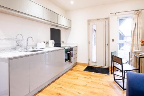a kitchen with white cabinets and a wooden floor at Three Tuns Apartments - Ash in Pettistree