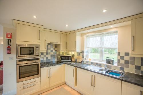 uma cozinha com armários brancos, um lavatório e uma janela em 2 Hazelwood em Aldringham