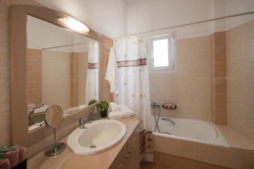 ein Badezimmer mit einem Waschbecken, einer Badewanne und einem Spiegel in der Unterkunft Veldi Art - Kamari Beach Apartment in Fira