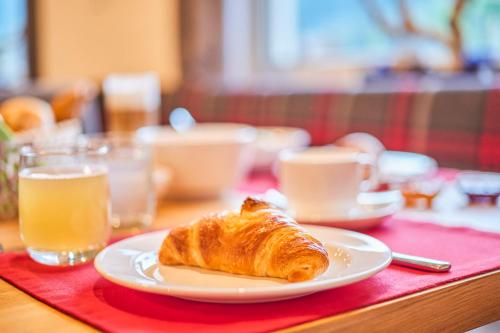 a plate with a croissant on a table with drinks at Kedul Lodge in Santa Cristina in Val Gardena