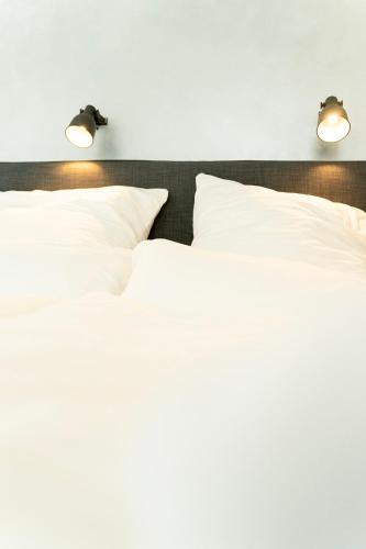 two beds with white pillows and two lights on the wall at City Apartments Hannover in Hannover