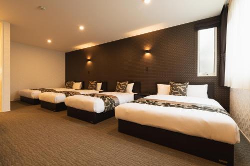 a hotel room with three beds and a window at GRAND BASE Nagasaki Ekimae in Nagasaki