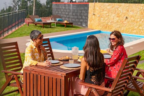 a group of people sitting at a table by a pool at Vilas Felicidade Rocha by An Island Apart in Ponta do Pargo