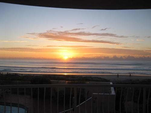 a sunset at the beach with people walking on the beach at Albatross North Apartments in Gold Coast