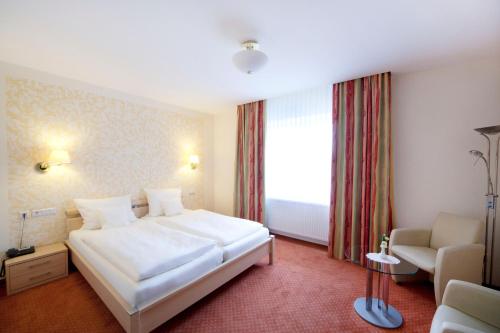 a bedroom with a white bed and a chair and a window at City-Hotel in Friesoythe
