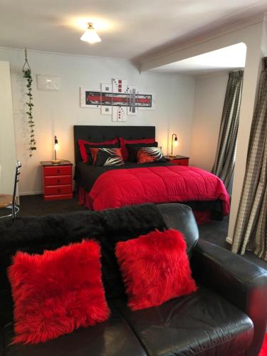 a bedroom with a bed with red pillows and a couch at Hideaway - A Couples Retreat in Akaroa