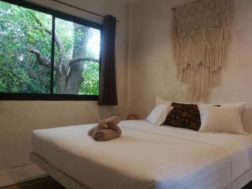 a teddy bear sitting on a bed with a window at DG House in Thongsala