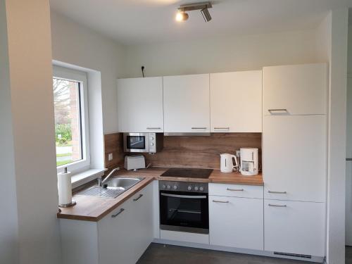 a kitchen with white cabinets and a sink and a window at Strandläufer in Butjadingen OT Tossens
