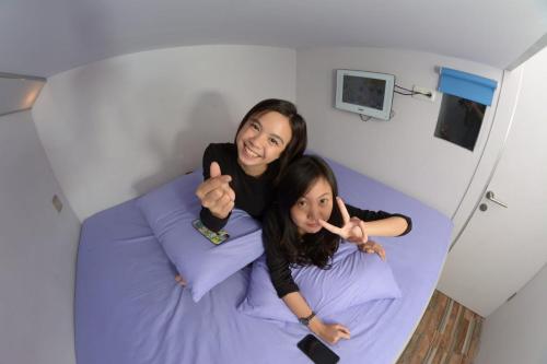 two girls sitting on a bed giving the thumbs up at Budi House & Food Station in Bandung