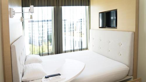 a bedroom with a white bed with a tv and a window at Sound Garden Hotel Airport in Warsaw
