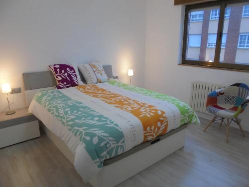 um quarto com uma cama, uma cadeira e uma janela em Jaen Apartment em Ponferrada