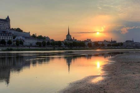 einen Sonnenuntergang über einer Stadt mit einer Reflexion im Wasser in der Unterkunft Appartement de charme bord de Loire in Saumur