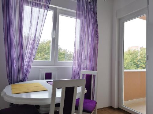 ein Esszimmer mit lila Vorhängen sowie einem Tisch und Stühlen in der Unterkunft Apartman Alto in Belgrad