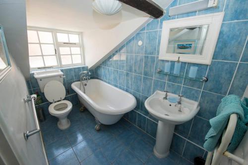 a blue tiled bathroom with a toilet and a sink at Buttercup Cottage in Holt