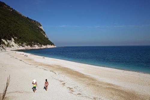 two people walking on a beach next to the ocean at La Piana Affittacamere in Camerano